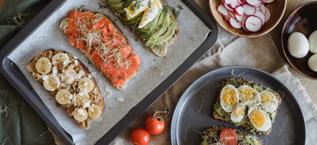 A variety of savory and sweet toasts with avocado, banana, eggs, and fresh toppings on a wooden table.