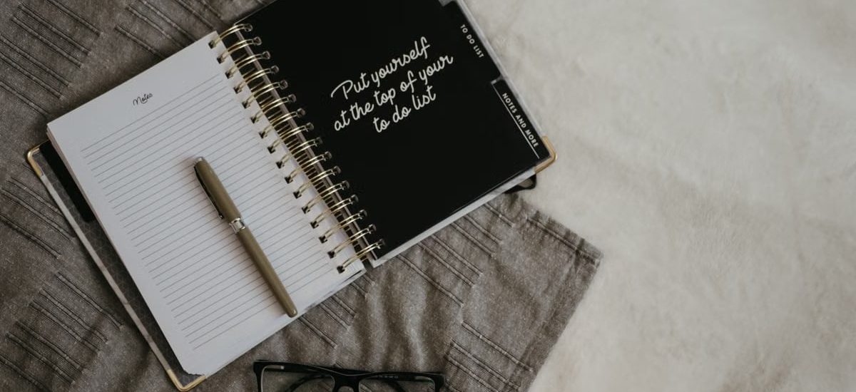 Stylish flatlay featuring a planner with quote, pen, and eyeglasses on a neutral background.