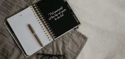 Stylish flatlay featuring a planner with quote, pen, and eyeglasses on a neutral background.