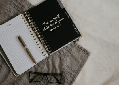 Stylish flatlay featuring a planner with quote, pen, and eyeglasses on a neutral background.